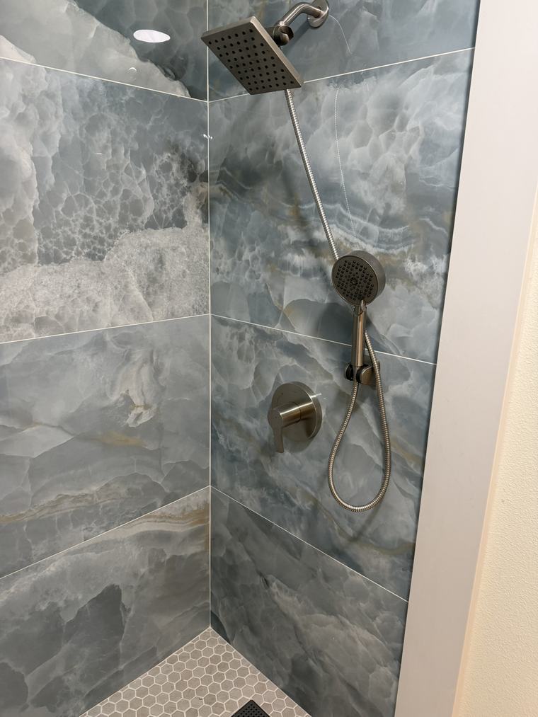 Detail of brushed nickel shower fixtures on marble slab tile