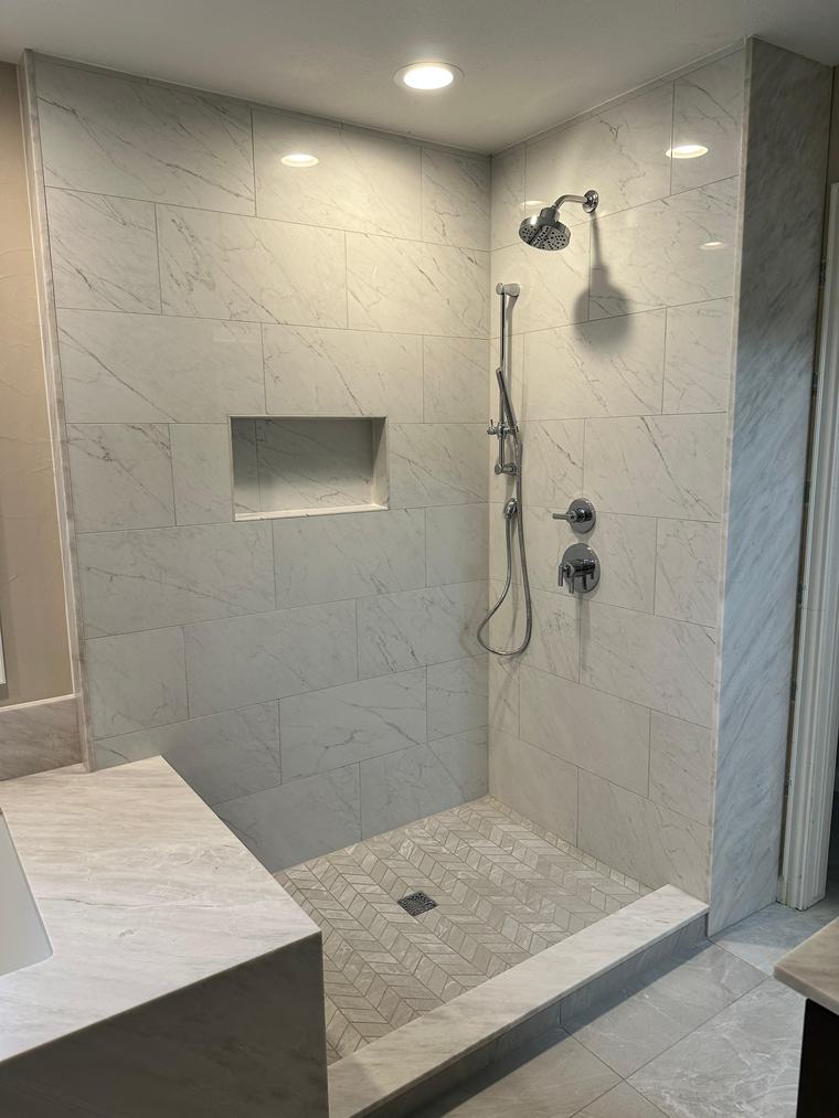 White marble shower with tile niche and herringbone mosaic floor