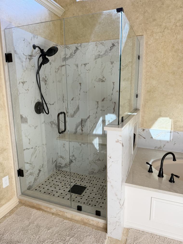 Frameless shower with oil-rubbed bronze fixtures, marble bench, and mosaic floor next to a soaking tub