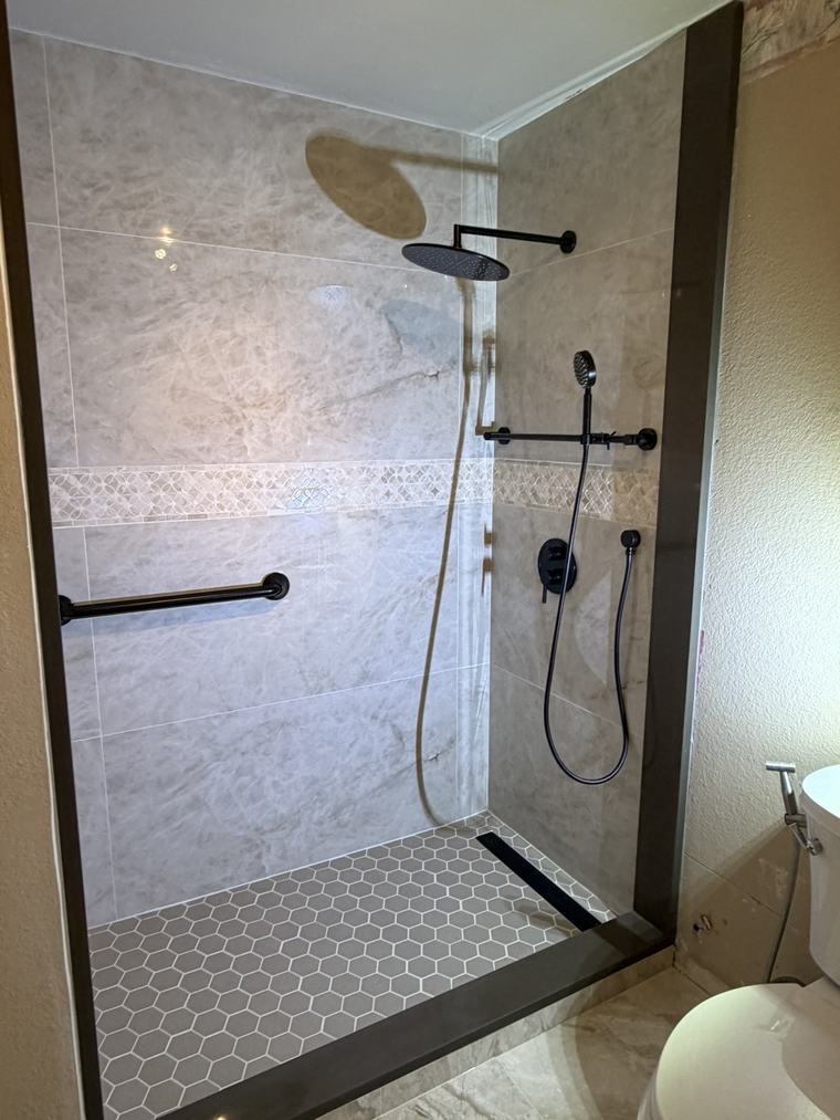 Accessible shower with black grab bar, black fixtures, and hexagon mosaic floor