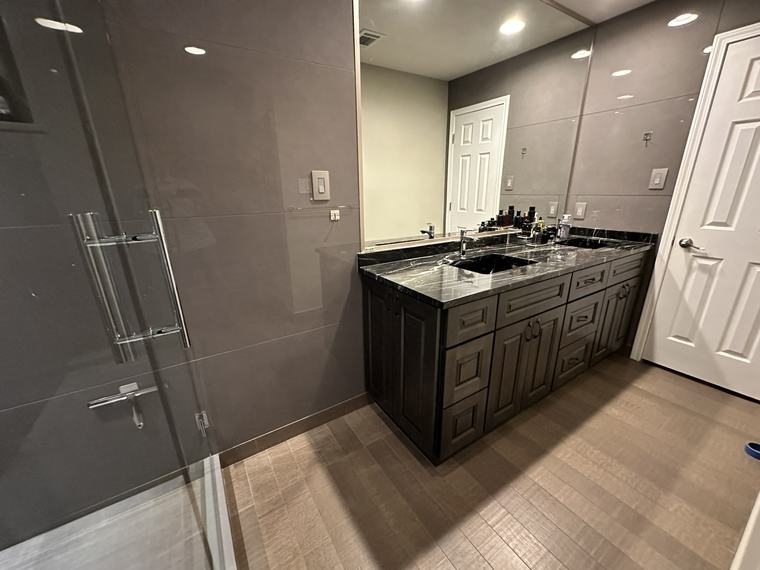 Dark tile shower reflecting a double-sink vanity with black marble countertop